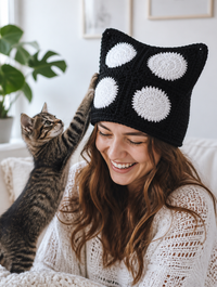 Woman laughing wearing the circle-pattern crochet cat-ear beanie while a kitten paws at it
